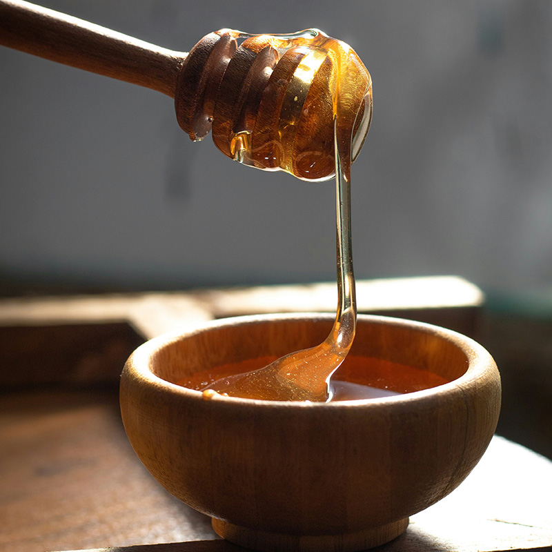 Honey drizzling from a wooden honey dipper into a wooden bowl
